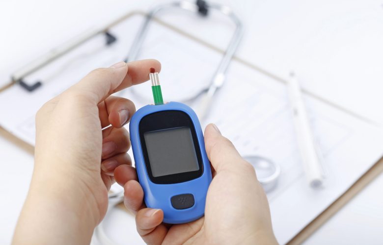 hand-holding-blood-glucose-meter-measuring-blood-sugar-background-is-stethoscope-chart-file-scaled.jpg